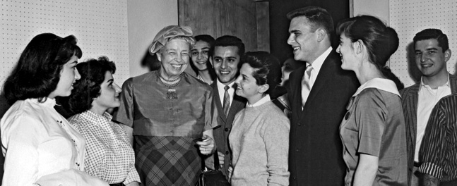 A smiling Eleanor Roose­velt standing among a group of students on campus in 1958.